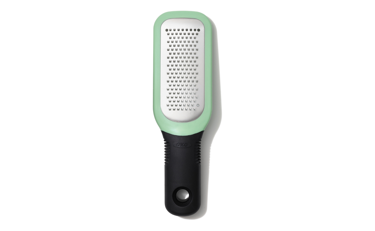 OXO Good Grips Etched Ginger & Garlic Grater with stainless steel etched teeth, soft grip handle, and snap‑on scraper cover shown in a modern kitchen setting.